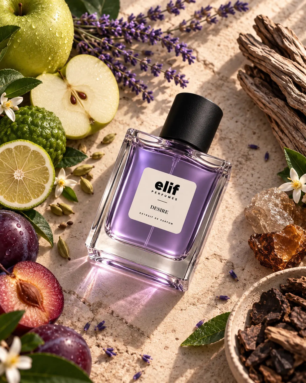 A rectangular glass perfume bottle with a black cap and a white label reading 'Elif Perfumes DESIRE' sits on a textured stone surface surrounded by green apples, sliced fruit, purple flowers, lime, bark, and dried botanicals.