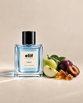 Elif Frost perfume bottle filled with translucent icy blue liquid and topped with a glossy black cap, displayed against a warm beige background. A green apple, sliced green apple, dark purple plums, and golden amber resin are arranged beside the bottle, with fresh water droplets, soft directional lighting, and subtle shadows.