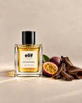 Elif Oud Molissima perfume bottle filled with warm golden liquid and topped with a glossy black cap, displayed against a warm beige background. A sliced passion fruit, dark plum, oud wood pieces, green leaves, and a brown leather-like material are arranged beside the bottle, with warm directional lighting and subtle shadows.