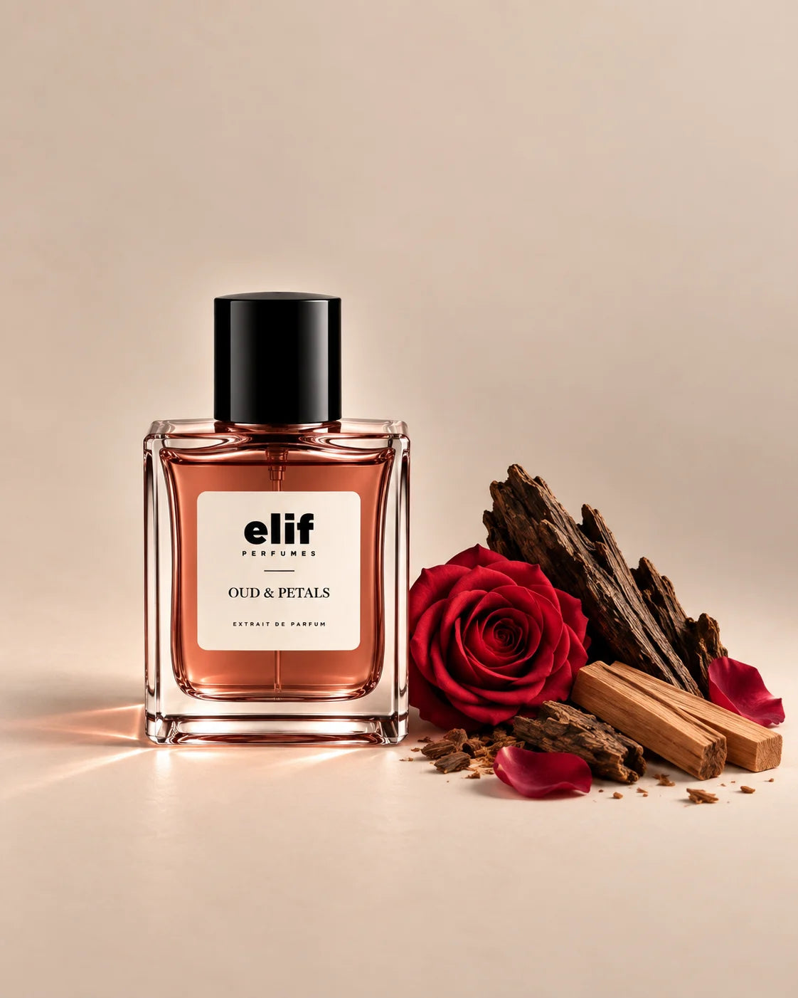 Elif Oud & Petals perfume bottle with a warm rose-toned liquid and glossy black cap, set against a soft beige background. A deep red rose, scattered rose petals, dark oud wood, and light-colored sandalwood pieces are arranged beside the bottle, with warm directional lighting and soft shadows. A long-lasting fragrance with a rich, woody, rosy, and luxurious character.