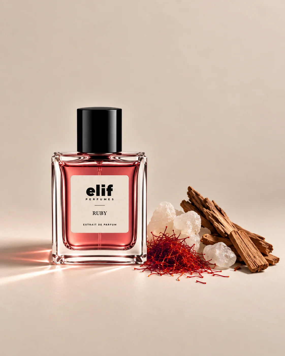 Elif Ruby perfume bottle filled with translucent ruby-red liquid and topped with a glossy black cap, displayed against a warm beige background. Saffron threads, pale amber resin crystals, and dark oud wood are arranged beside the bottle, with warm directional lighting and subtle shadows.