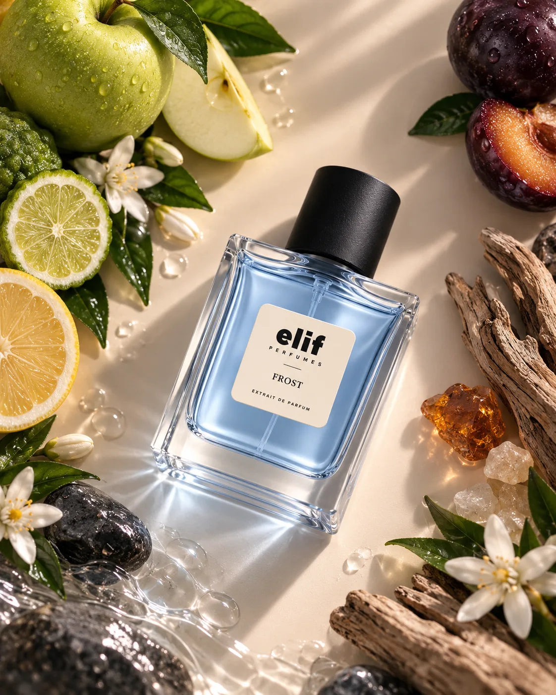 A bottle of Elif Perfumes FROST Extrait de Parfum is displayed on a light beige surface surrounded by fresh green apples, sliced limes, plums, white flowers, crystals, and pieces of driftwood. The product is a square glass bottle with light blue liquid and a black cap.