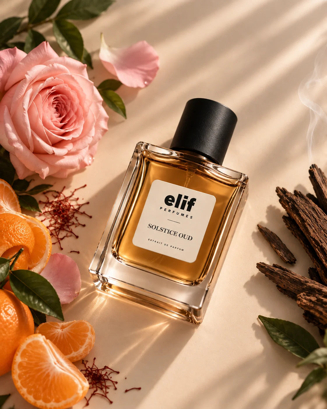 A bottle of Elif Perfume 'Solstice Oud' with amber liquid and a black cap, styled on a beige surface with a pink rose, orange slices, green leaves, and dried bark under soft diagonal shadows.