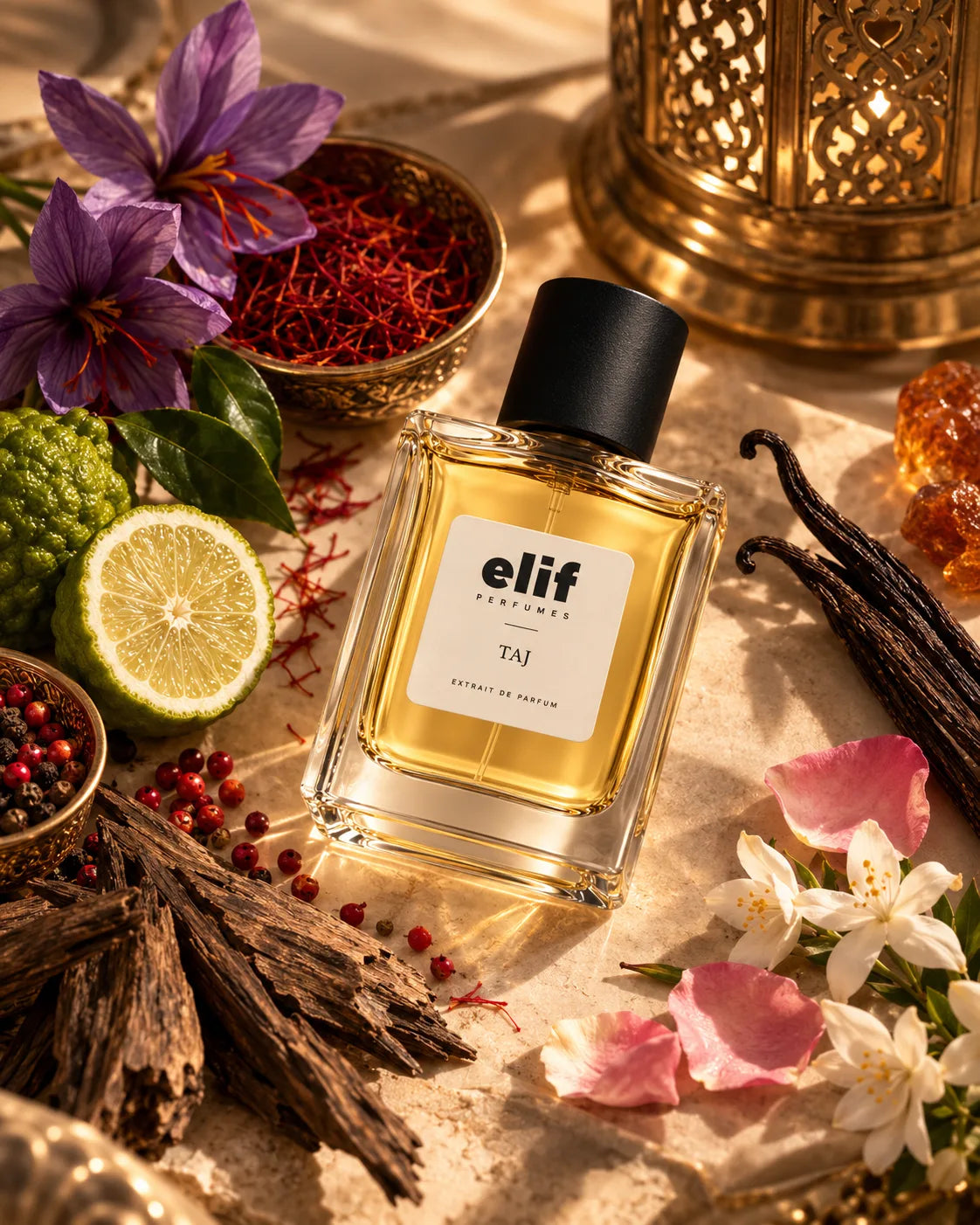 A bottle of elf perfume with a black cap and a white label reading 'Elif perfume TAJ', surrounded by saffron, purple flowers, a lime slice, vanilla beans, amber crystals, and dried roots on a warm neutral surface.